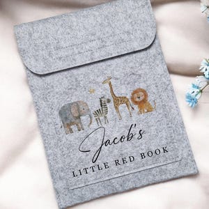 May include: A gray felt book cover with a flap closure. The cover features watercolor illustrations of an elephant, zebra, giraffe, and lion. The text "Jacob's Little Red Book" is printed on the front.