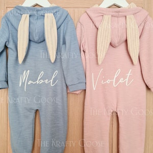 May include: Two baby bunny-themed hooded onesies, one blue with the name "Mabel" and one pink with the name "Violet" embroidered on the back.
