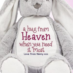 May include: A grey plush bunny with long ears and white accents on the paws and inner ears. The bunny has embroidered text on its chest that reads "a hug from Heaven when you need it most".