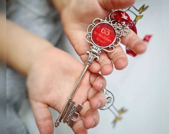 May include: A decorative silver key with a red circular centerpiece. The centerpiece has the number 63 and the text "St Andrews Road". The key is held in a person's hands. The key has the word "HOHOHO" on the key's teeth.