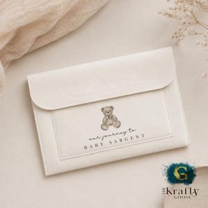 May include: A cream-coloured baby keepsake envelope with a flap closure. A watercolour illustration of a teddy bear with a bow tie is centered on the front, with the text "our journey to BABY SARGENT" below. The Kraftly Goose logo is in the bottom right corner.