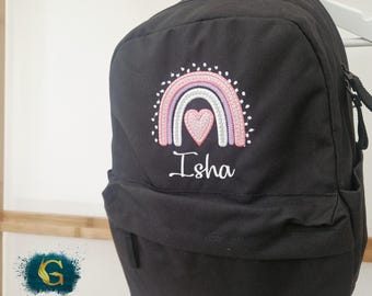 May include: Black backpack with a rainbow and heart design embroidered in pink, white, and light pink. The name "Isha" is embroidered below the rainbow. The backpack has a front pocket and a top handle.