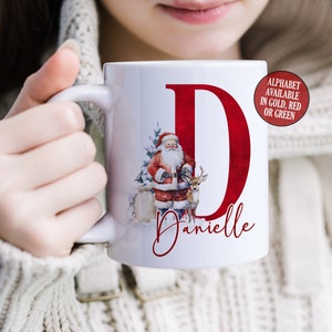 May include: White ceramic mug with a red letter D, a Santa Claus illustration, and the name Danielle. The letter D is available in gold, red, or green.