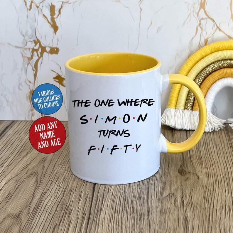 May include: White ceramic mug with a yellow interior and handle. The mug features the text "THE ONE WHERE SIMON TURNS FIFTY" in black, with the name "SIMON" in the style of the TV show "Friends". Additional text on the mug includes "VARIOUS MUG COLOURS TO CHOOSE" and "ADD ANY NAME AND AGE".