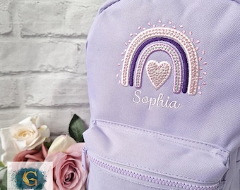 May include: A lavender backpack with a rainbow and heart embroidery design. The rainbow features shades of purple and pink, with the name "Sophia" embroidered below. The backpack has a front zippered pocket and a top handle.
