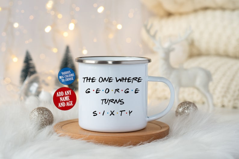May include: White enamel mug with a silver rim, featuring the text "THE ONE WHERE GEORGE TURNS SIXTY" in black, with the name in colorful letters. The mug sits on a wooden coaster, with decorative elements in the background.