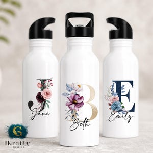 May include: Three white water bottles with black lids, each decorated with a floral initial and name. The initials are "J", "B", and "E", with the names "Jane", "Beth", and "Emily" in script. The floral designs include pink, purple, and blue flowers.