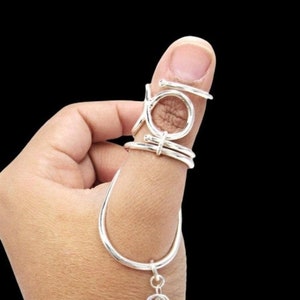Puede incluir: Anillo de pulgar de plata con un diseño único que presenta múltiples círculos entrelazados. El anillo está unido a una cadena de plata con un dije.