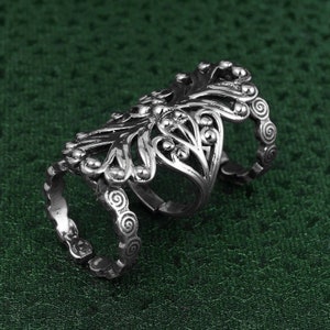 May include: A silver filigree ring with a double band design. The ring has a floral pattern with intricate details.