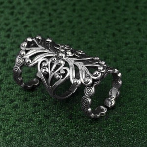 Puede incluir: Un anillo de filigrana plateado con un delicado diseño floral. El anillo es ajustable y se puede llevar en varios dedos.