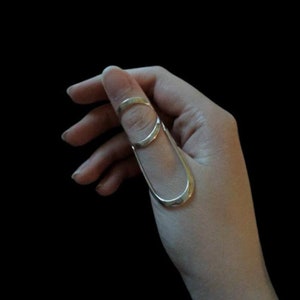 Puede incluir: Un anillo de pulgar de plata con un diseño abierto único. El anillo está hecho de dos bandas superpuestas, creando un aspecto moderno y minimalista.