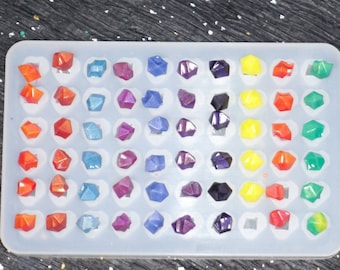 Puede incluir: Un molde de silicona con 60 cavidades individuales, cada una con forma de pequeña gema puntiaguda. El molde está lleno de resina de colores, creando un efecto de degradado arcoíris.
