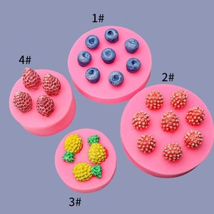 May include: Four silicone moulds for making fruit-shaped sweets. The moulds are pink and feature different fruits: blueberries, raspberries, strawberries, and pineapples. The moulds are labelled with numbers 1 through 4.