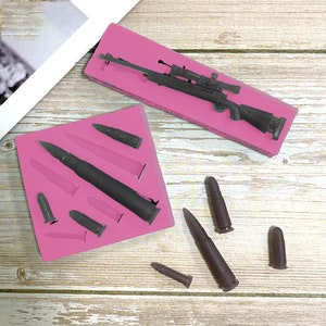 May include: Pink silicone mold with a rifle and bullets. The mold is on a wooden surface. There are also several bullets outside of the mold.