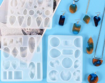 May include: Three clear silicone molds for making resin jewelry. The molds are filled with various shapes, including circles, ovals, and teardrops. There are also several finished resin pieces in blue, brown, and gold colors.