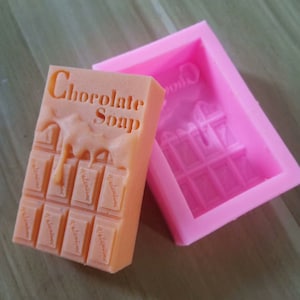 May include: Orange silicone mold for making chocolate soap bars. The mold is shaped like a chocolate bar with the words "Chocolate Soap" embossed on the top.
