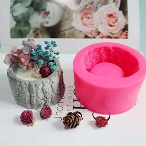 May include: A pink silicone mould for making a concrete candle holder. The mould is shaped like a tree trunk with a round top. The mould is next to a finished concrete candle holder with dried flowers inside.