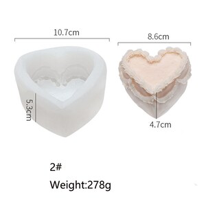 K&ouml;nnte beinhalten: Eine wei&szlig;e Silikonform in Herzform zum Herstellen von Bastelarbeiten oder Desserts. Die Form ist 10,7 cm breit, 5,3 cm hoch und 8,6 cm lang. Die Form ist neben einem rosafarbenen herzf&ouml;rmigen Objekt zu sehen, das 4,7 cm breit ist. Der Text "2# Gewicht: 278 g" ist unter der Form aufgedruckt.