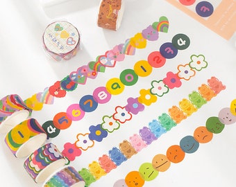 Puede incluir: Surtido de cintas adhesivas washi de colores con diferentes diseños. Las cintas presentan arcoíris, corazones, flores, números, osos y caras sonrientes.