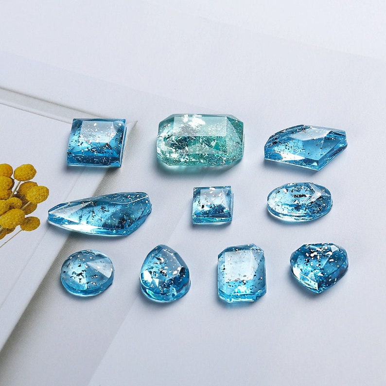 Pode incluir: Conjunto de gemas de resina azul e verde com acabamento brilhante. As gemas s&atilde;o de v&aacute;rias formas, incluindo quadrada, oval, de l&aacute;grima e retangular.