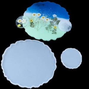 May include: Three silicone molds for resin art projects. The molds are in the shape of irregular circles with wavy edges. The largest mold is light gray, the medium mold is light blue with white flowers and green leaves, and the smallest mold is light gray.
