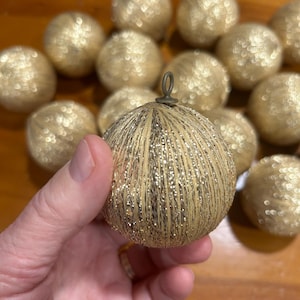 May include: A collection of gold Christmas ornaments with a sparkly, textured finish. The ornaments are round and have a metallic sheen.