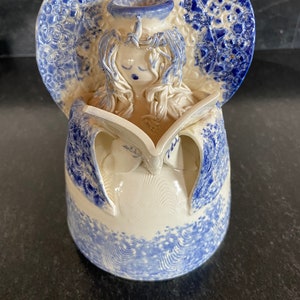 May include: A ceramic angel figurine with blue and white glaze. The angel is holding a book and has a halo.