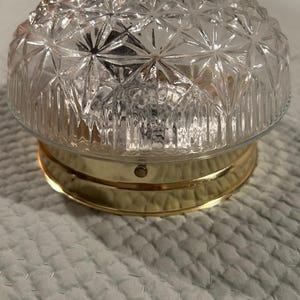 May include: A clear glass ceiling light fixture with a brass base and a geometric pattern. The glass is textured with a diamond pattern.