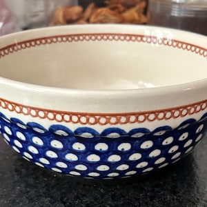 May include: Ceramic bowl with a cream-colored interior and a blue and white dotted pattern on the exterior. The rim features a brown decorative border. A decorative piece for the kitchen.