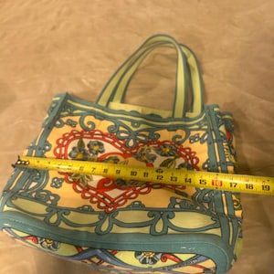 May include: A patterned tote bag with a heart design. The bag is approximately 16 inches wide. It features a yellow background with a floral and scroll design in red, blue, and green. The handles are light green.