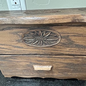 May include: A wooden box with a carved sunflower design on the front. The box has a drawer on the bottom.