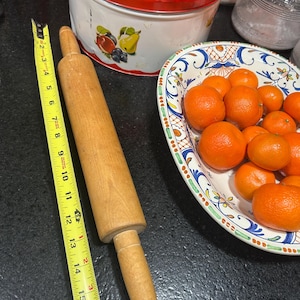 May include: A wooden rolling pin with a natural finish and a handle on each end. The rolling pin is 15 inches long.