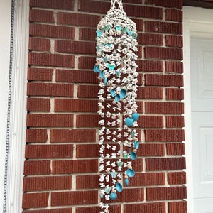 May include: A white and blue seashell wind chime with a decorative top. The chime is made of various sized seashells and blue butterflies.