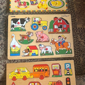 May include: Three wooden jigsaw puzzles. The top puzzle has a Christmas theme. The middle puzzle is farm-themed, with a cow, tractor, and pig. The bottom puzzle features vehicles like cars and a bus. Made in Holland.