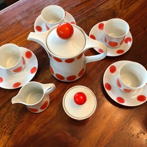 May include: A white teapot with orange polka dots and a matching sugar bowl, creamer, and four teacups and saucers. The teapot has a red knob on the lid. The teacups and saucers have a white background with orange polka dots.