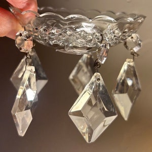 May include: A set of clear glass crystal prisms hanging from a small, scalloped, clear glass base. The prisms are diamond-shaped and have a faceted design.