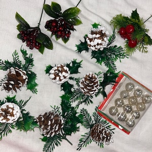 May include: Assortment of Christmas decorations including pine cone sprigs, holly sprigs, red berry sprigs, and a box of silver ornaments.