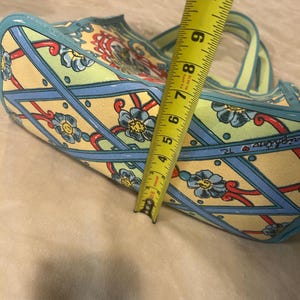 May include: A patterned tote bag with a floral design in yellow, blue, and red. The bag has a light blue trim and handles. The bag is approximately 7 inches wide.