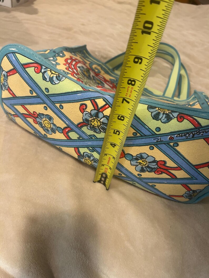 May include: A patterned tote bag with a floral design in yellow, blue, and red. The bag has a light blue trim and handles. The bag is approximately 7 inches wide.