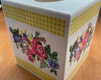 May include: White ceramic tissue box cover with a yellow and white checkered pattern and a floral design featuring pink, purple, and yellow flowers.