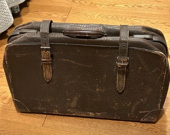 May include: A vintage brown leather suitcase with two buckles and a handle. The suitcase has a worn and distressed look.