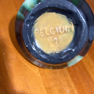 May include: Close-up of the bottom of a green and brown glazed ceramic pot with the word "DELICIOUS" stamped in gold on the bottom.