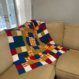 May include: A multi-colored patchwork throw blanket with squares of red, blue, green, white, and orange. The blanket is draped over a brown couch.