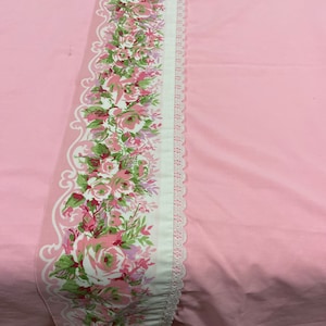 May include: Pink bedding with a white lace trim and a floral pattern. The floral pattern features pink, white, and green roses.