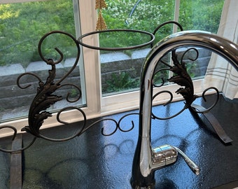 May include: A black metal stand with a circular top and ornate scrollwork. A chrome faucet is attached to the stand.