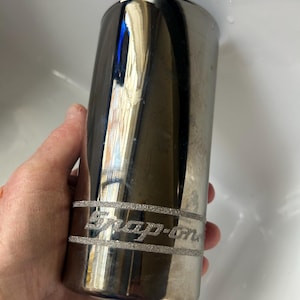 May include: A cylindrical, chrome-plated Snap-on tool. The tool has a silver band with the Snap-on logo etched in a textured, glittery style. The tool is held in a hand.