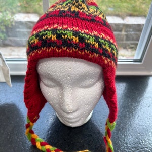 May include: Red knitted hat with a black, yellow, and green pattern. The hat has a long braided tassel.