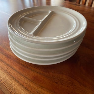 May include: A stack of five white ceramic divided plates. The plates have a raised rim and a smooth, glossy finish.