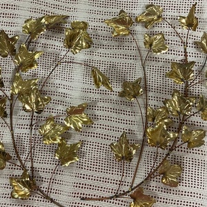 May include: Two gold metal ivy vines with leaves, arranged in a circular shape on a white background.