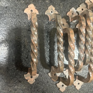 May include: A set of ten rustic, twisted metal drawer pulls with a decorative, pointed design. The pulls are a dark brown color with a hint of rust.